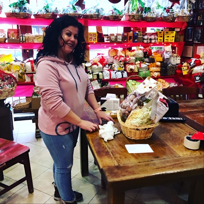 Woman smiling in Tino's Delicatessen, surrounded by Italian deli products and gift baskets.