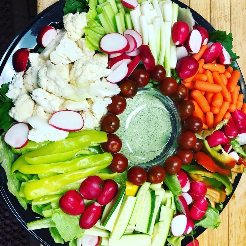 A large platter of fresh vegetables including cauliflower, radishes, carrots, and bell peppers with a dip.
