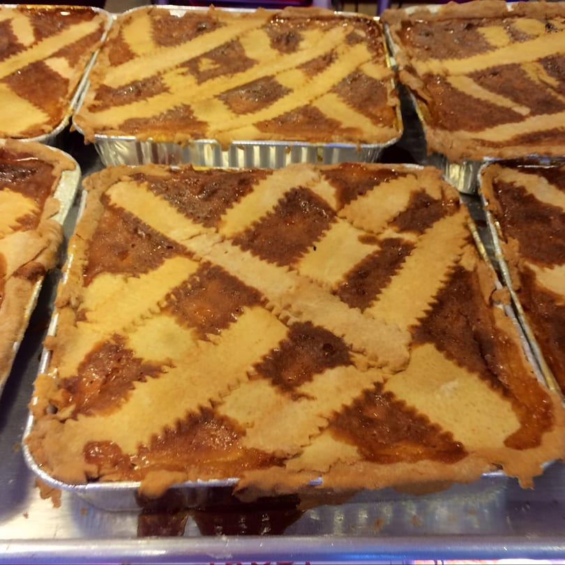 Several Italian deli pastries with lattice tops and a sweet, dark filling in foil pans.