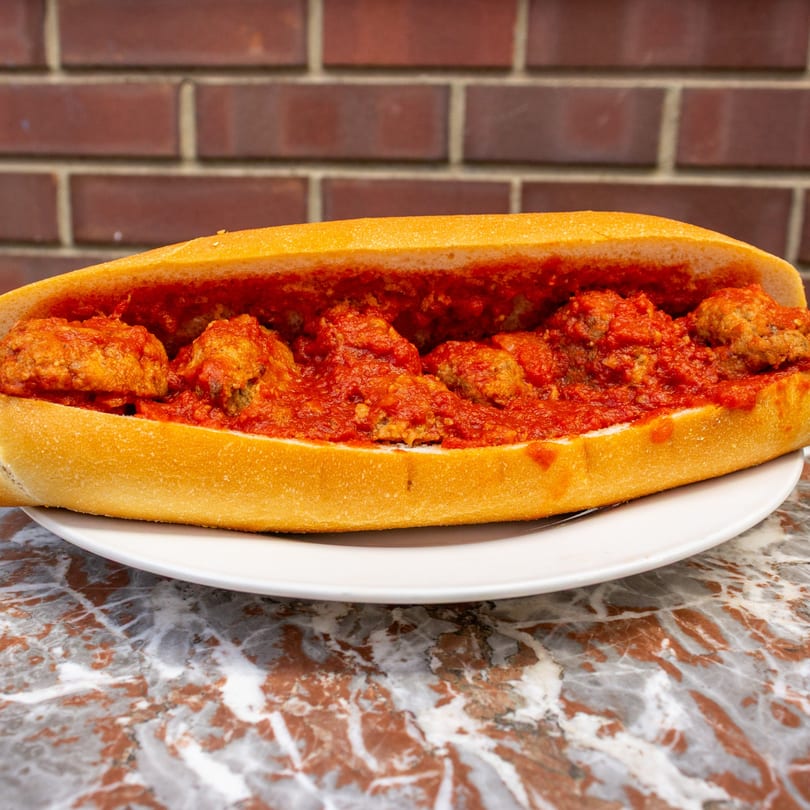 A Tino's Delicatessen meatball hero, overflowing with meatballs and red sauce, on a white plate.