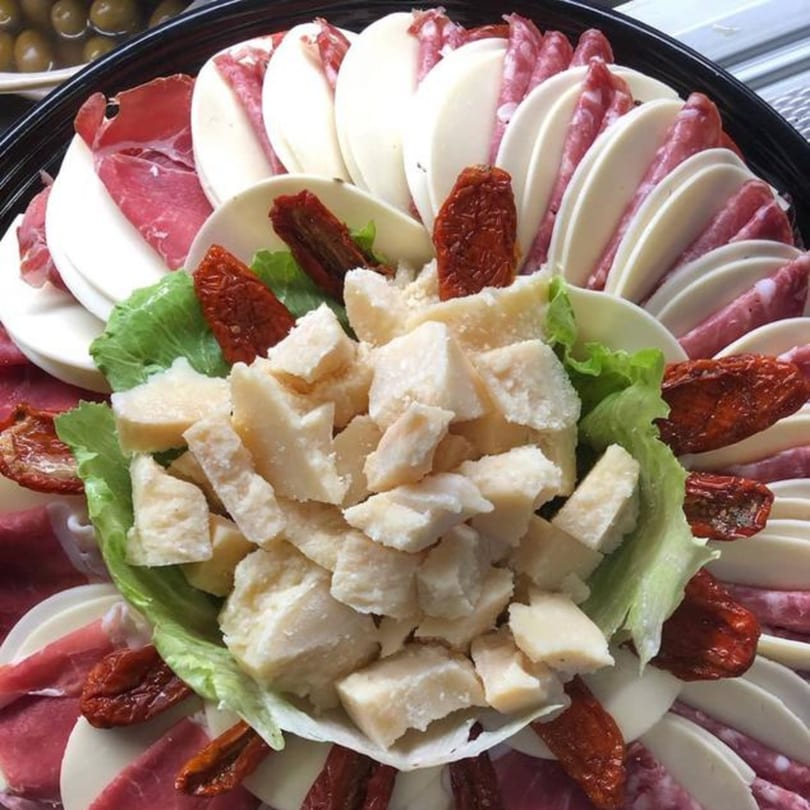 A Tino's Delicatessen platter with sliced meats, cheeses, sun-dried tomatoes, and Parmesan chunks.