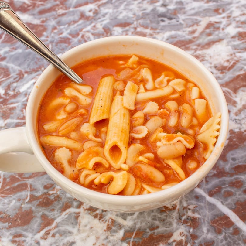 Hearty Tino's Delicatessen pasta e fagioli soup with beans and various pasta shapes in a mug.