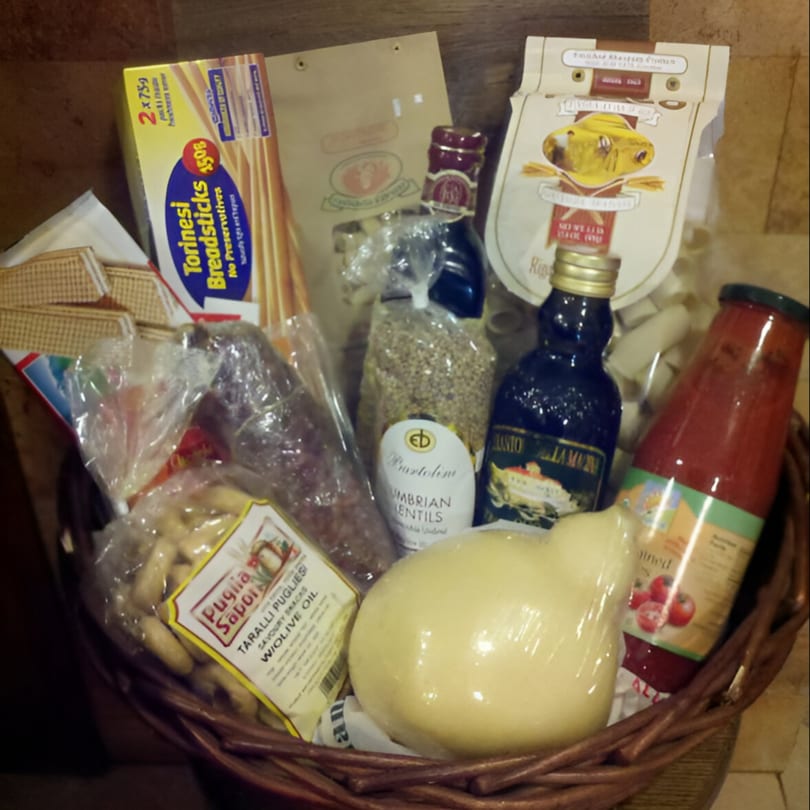 A Tino's Delicatessen gift basket filled with Italian breadsticks, pasta, lentils, olive oil, and cheese.