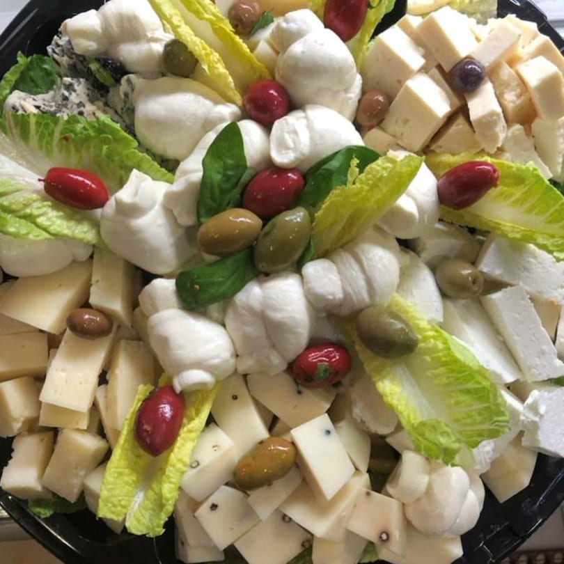 A platter of fresh mozzarella balls, cubed cheeses, olives, and lettuce at Tino's Delicatessen.